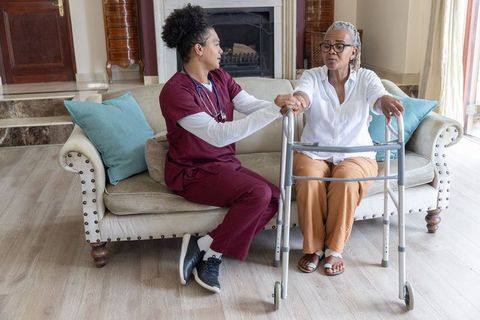 Home nurse helping senior african-american woman using walker, providing mobility support