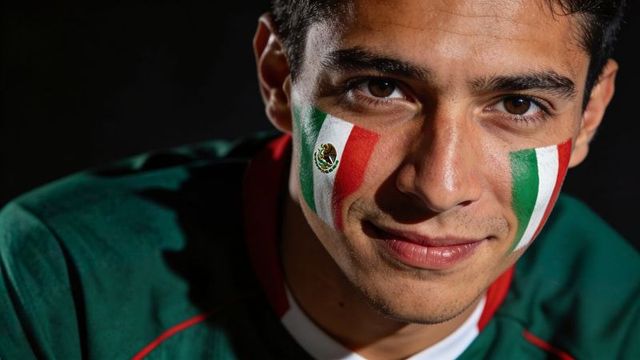 Young mexican fan wearing tricolor face paint and green jersey celebrating football victory