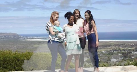 Friends enjoying coastal terrace with baby, smiling and chatting against ocean view