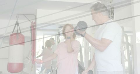 Senior couple exercising with dumbbells in bright gym, strength training partnership