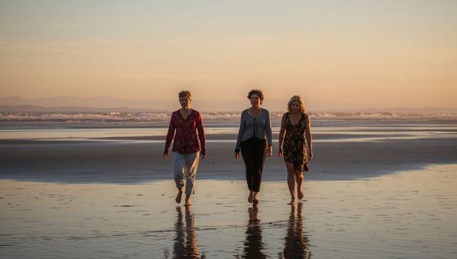Three women walking on sunset beach with reflective wet sand and distant waves