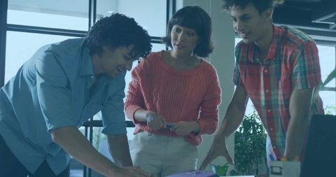 Young Team Reviewing Documents Around Desk Holding Pen and Purple Binder in Modern Office