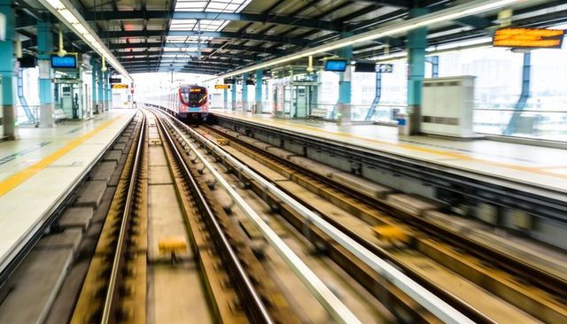 Red metro train approaching elevated station tracks with motion blur and urban perspective