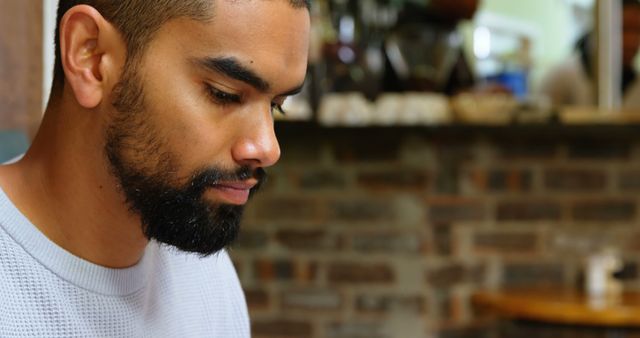 Young man with beard reading and concentrating in a cozy cafe environment. Implies focus, relaxation, and leisure in a modern indoor setting. Suitable for themes about studying, casual lifestyle, self-improvement, or coffeeshop culture.