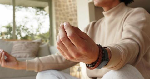 Male meditating in cozy living room with mudra hands, smartwatch and bracelets