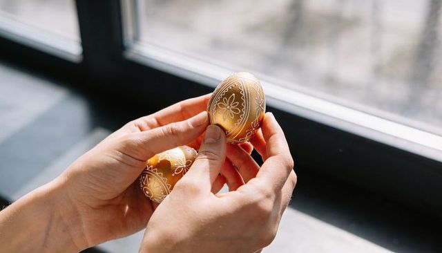 Hands holding ornate golden easter eggs with floral geometric pattern in sunlight