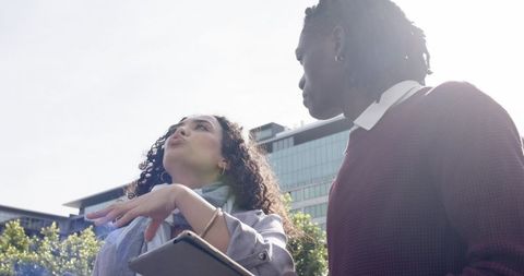 Diverse coworkers discussing project holding tablet beside glass office building backlit