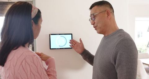 Father and daughter adjusting smart thermostat at home