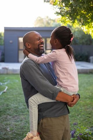 African american father holding laughing daughter in backyard garden joyful family moment