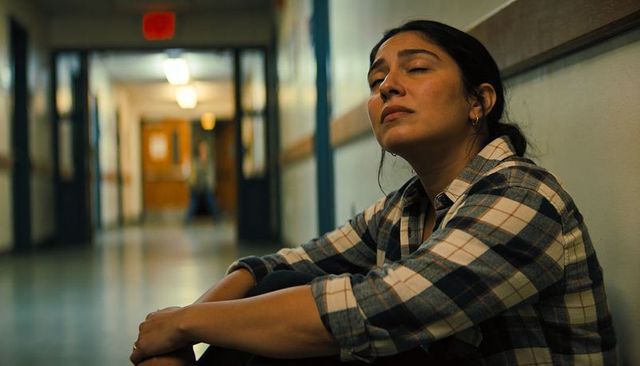 Young woman sitting in hallway wearing plaid flannel, contemplative fatigue and stillness