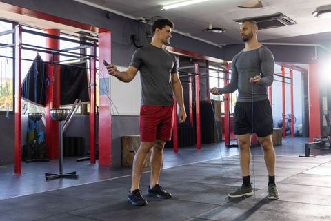 Two male training partners holding jump ropes chatting while standing on gym floor