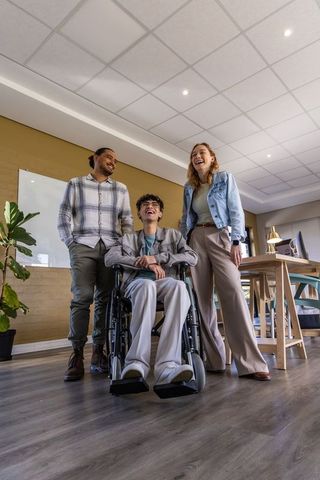 Diverse coworkers smiling and collaborating around wheelchair in modern office teamwork