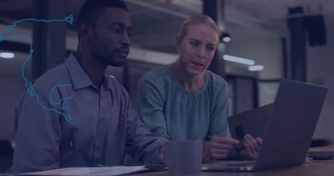 Two colleagues collaborating over laptop and tablet in modern open-plan office at desk