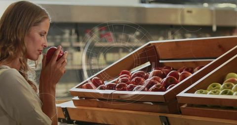 Woman smelling fresh red apple at supermarket produce display with wooden crates and futuristic hud