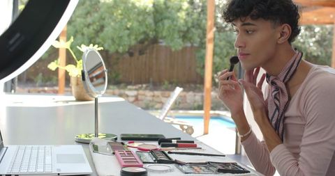 Man applying makeup beside pool with ring light on patio