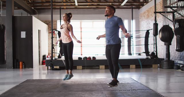 Image of fit diverse woman and man jumping on jumping rope at gym. active, fit, sporty and healthy lifestyle, exercising at gym concept.