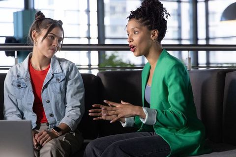 Diverse female coworkers collaborating on sofa with laptop in modern bright office lounge