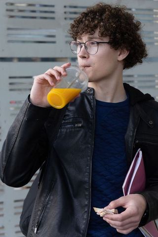 Teen sipping orange juice at transit stop holding notebook and snack