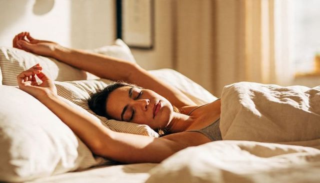 Sunlit morning woman stretching on bed with cozy neutral linens and soft pillows
