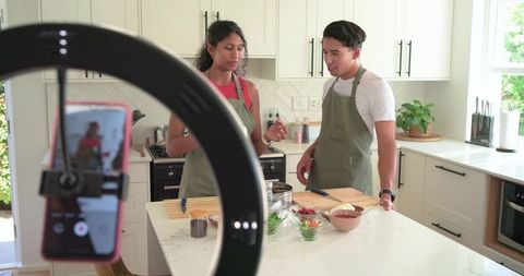 Couple preparing recipe on kitchen island filming with ring light and smartphone