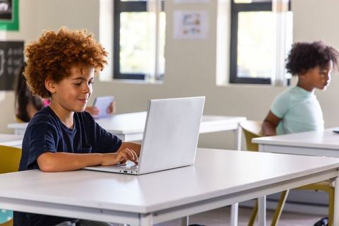 African American student using laptop in modern classroom focusing on remote learning and coding