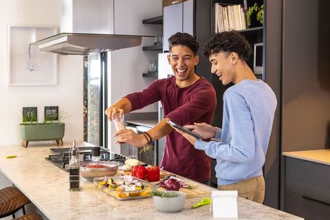 Hispanic male friends preparing meal at modern kitchen island