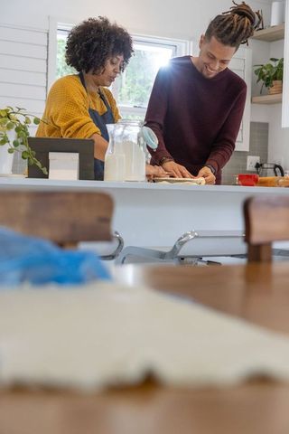 Couple baking together on sunlit kitchen island rolling dough sharing warm morning moment
