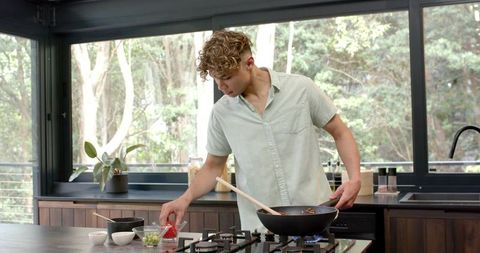 Young Man Cooking in Modern Home Kitchen with Wok on Gas Stove