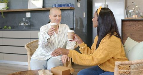 Diverse friends sharing coffee in cozy kitchen nook, black and shaved-head women