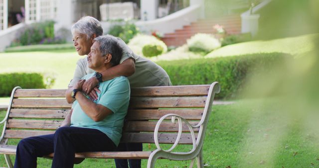 Image of happy biracial senior couple embracing and sitting on bench in garden. active retirement lifestyle, senior relationship and spending time together concept.