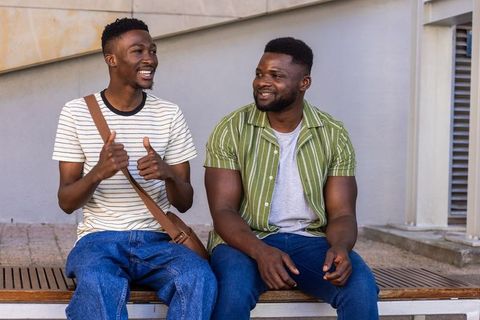 Two african american men laughing and chatting on bench in urban plaza casual friendship