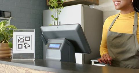 African american barista smiling and tapping pos screen at cafe counter with qr code sign
