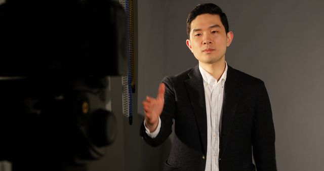 Young businessman interacting in a studio under professional lighting, dressed formally in a dark blazer and white shirt. Ideal for business presentations, corporate training materials, articles on leadership, communication skills tutorials, and usage in profile introductions for company websites or marketing materials.