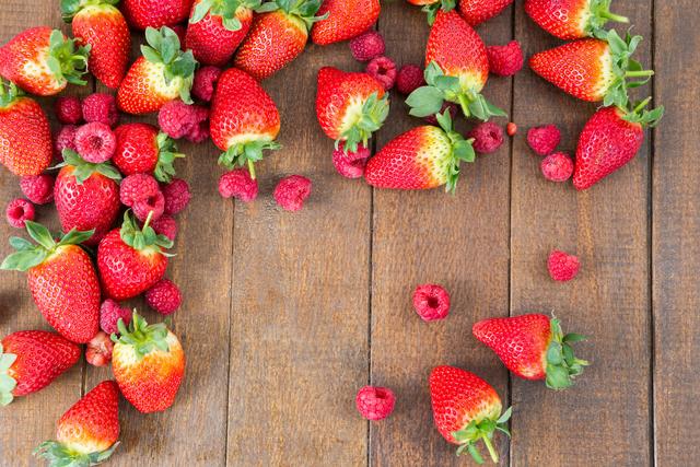 Fresh strawberries and raspberries arranged on wooden board