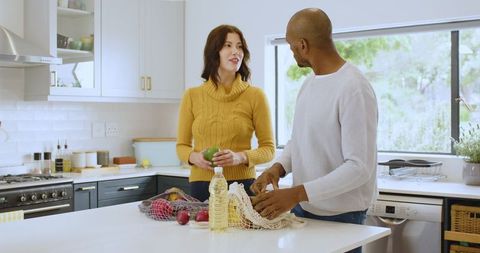 Couple organizing groceries in stylish kitchen with reusable bags