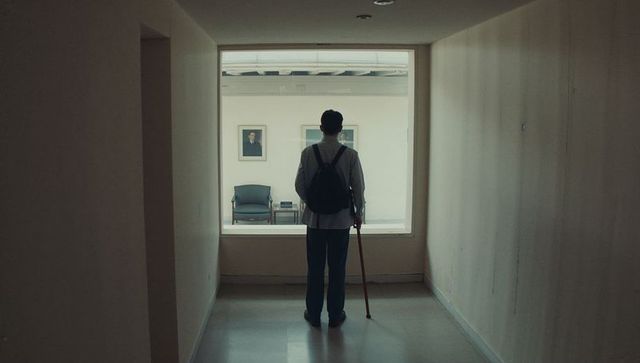 Solitary man standing with cane and backpack gazing through window into empty waiting room