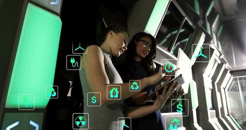 Diverse women analyzing tablet with augmented energy icons in futuristic green control hub