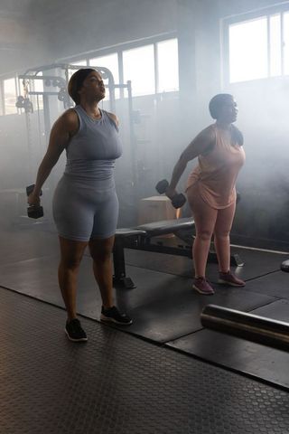 African american women lifting dumbbells together in gym strength training partner workout