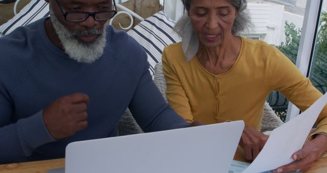 Biracial woman and African American man review documents at home. They're focused on managing finances or planning together indoors.