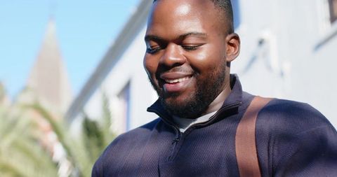 Smiling african american man wearing navy half-zip pullover and brown bag strap outdoors