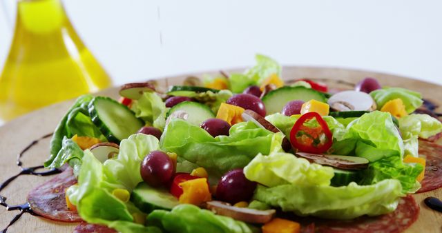 This vibrant image showcases a fresh organic salad with an assortment of vegetables including lettuce, cucumbers, tomatoes, and olives. The salad is topped with a light dressing, implied by the visible olive oil in the background. Ideal for promoting healthy eating, diet programs, vegetarian recipe books, and organic food product advertisements.