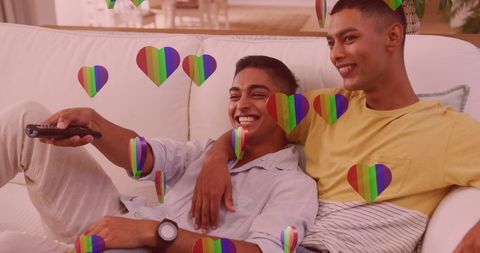 Smiling Male Couple Relaxing on Couch with Digital Rainbow Hearts