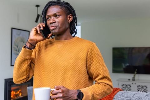 African american man talking on smartphone holding mug in mustard quilted sweatshirt