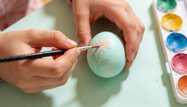 Child painting pastel mint easter egg with daisy design using fine brush and watercolors