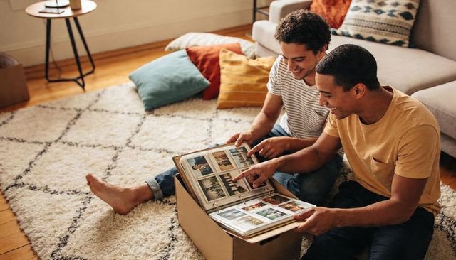 Two men reminiscing over memory album on living room floor, cozy home moment