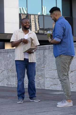 Casual urban coworkers sharing lunch and green smoothie while chatting in modern plaza