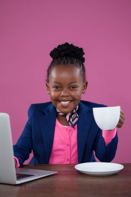 Portrait of smiling businesswoman having coffee at desk against pink wall in office