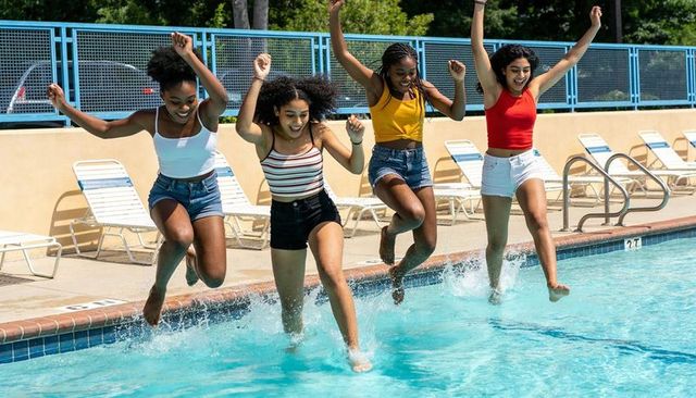 Jumping friends splashing at community pool during energetic summer youth celebration