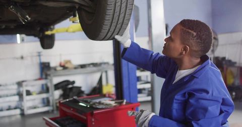 Young mechanic inspecting car wheel on lift in professional auto repair workshop
