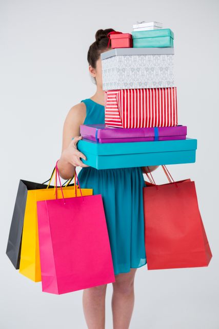 Woman carrying stack of gift boxes and shopping bags against white background